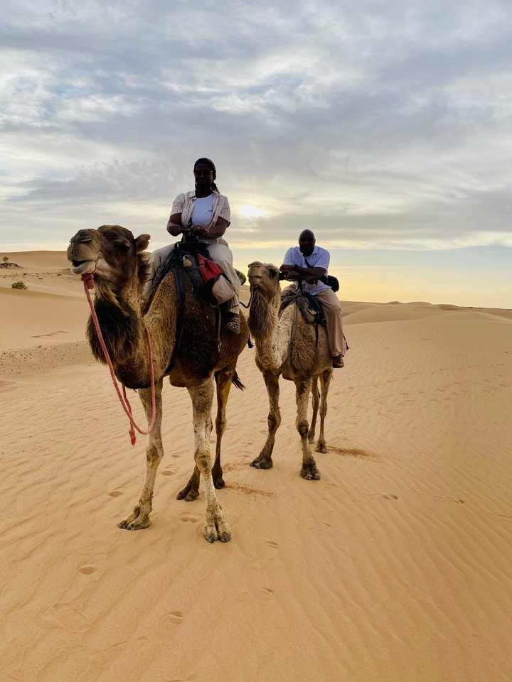 Deux personnes montant des chameaux dans un paysage désertique au coucher du soleil.