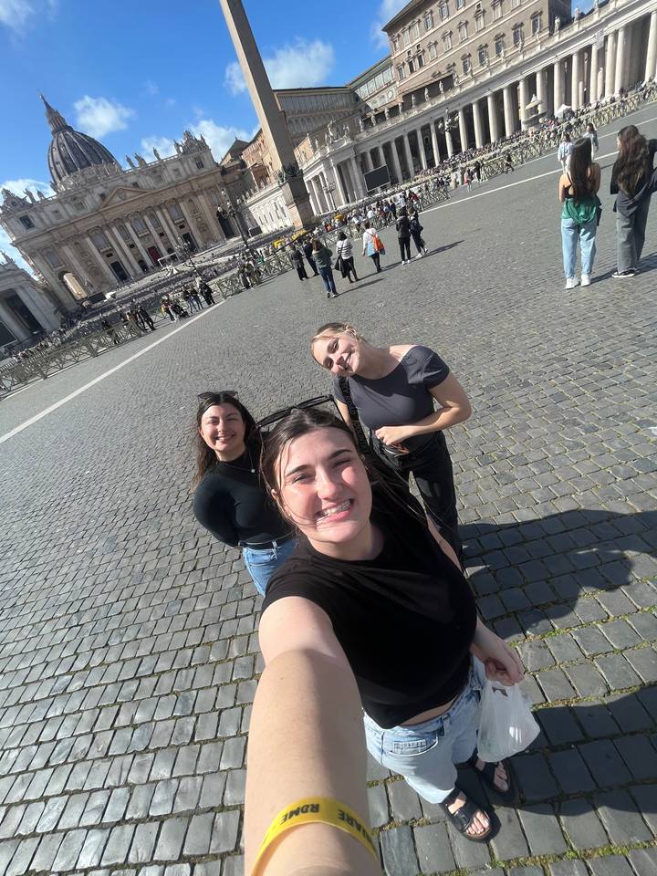 Trois personnes prenant un selfie devant une grande place avec des colonnes.