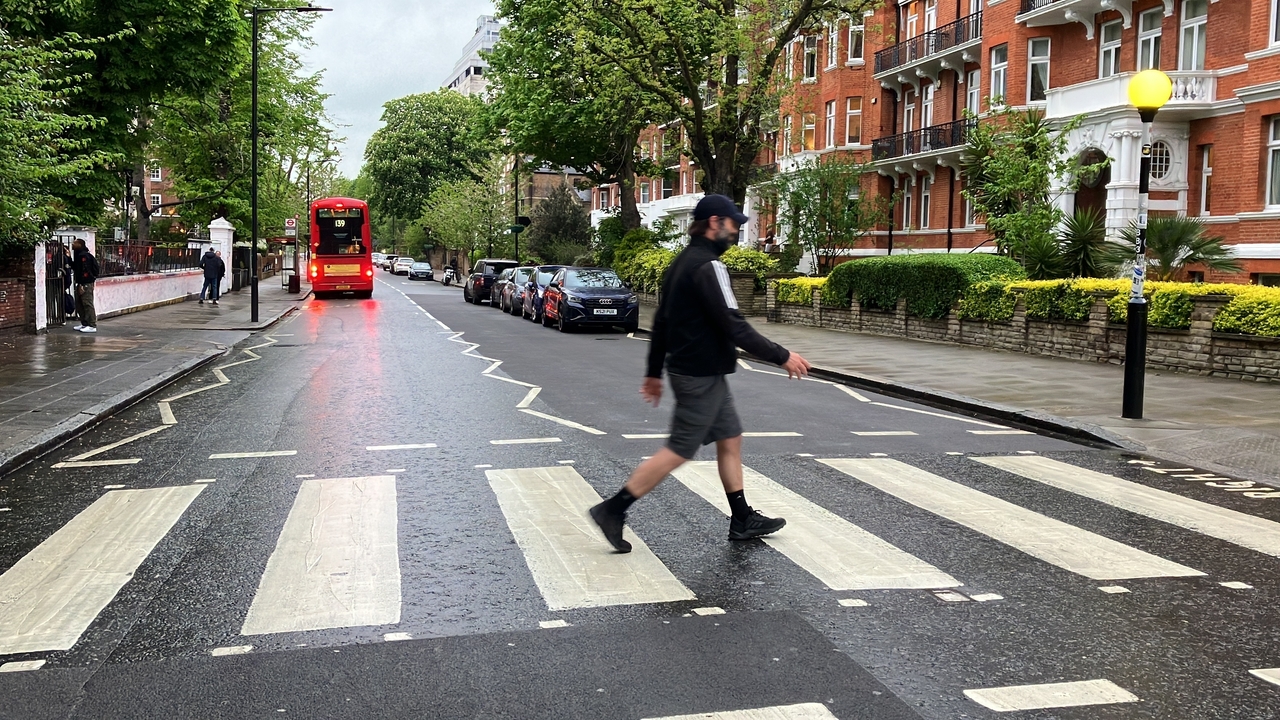 Persona cruzando un famoso paso de cebra con autobús rojo de dos pisos.