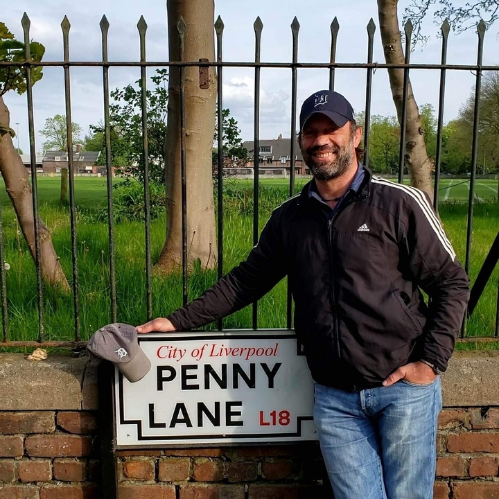 Hombre posando con un letrero en Liverpool, sonriendo ampliamente.