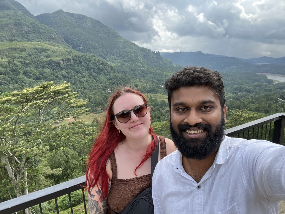 Couple prenant un selfie avec un paysage vallonné luxuriant en arrière-plan.