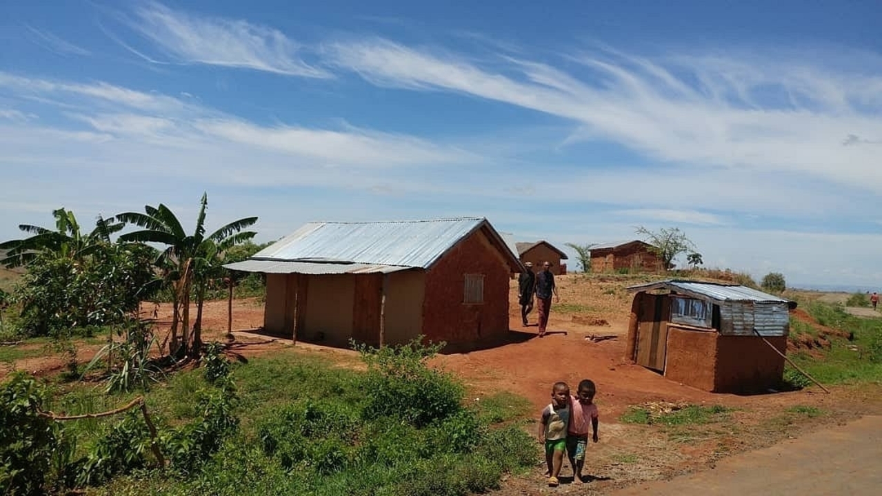 Plusieurs maisons simples et des gens dans une zone rurale avec un ciel bleu.