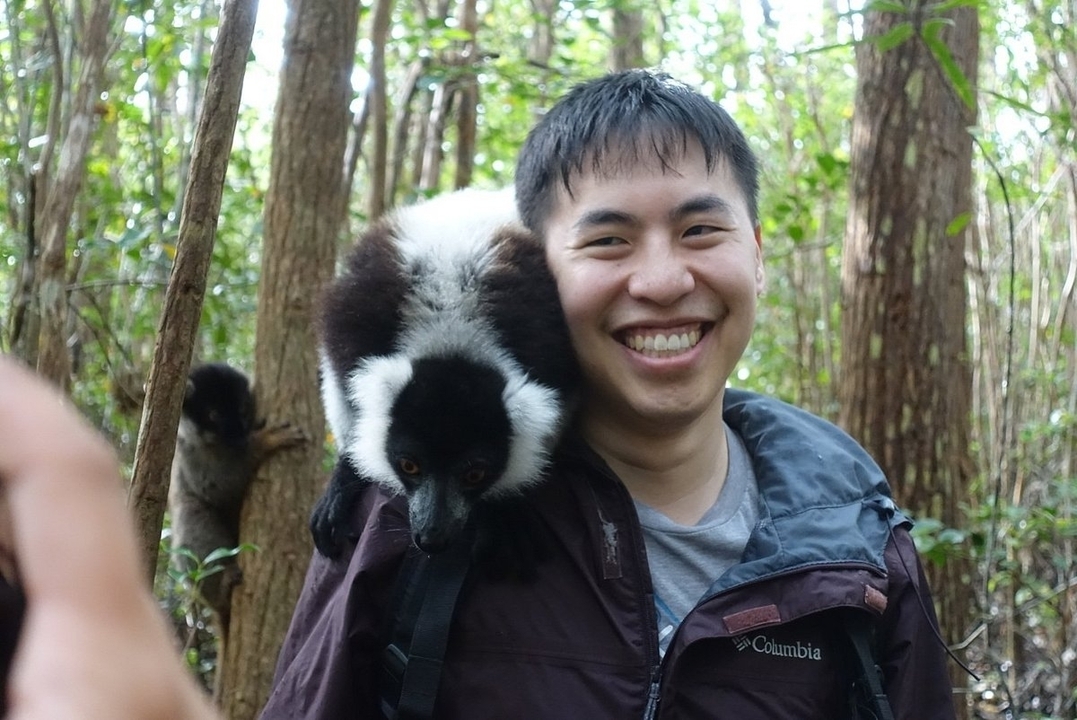 Personne avec un lémurien sur l'épaule dans un environnement forestier.