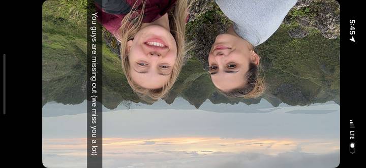 Deux femmes prenant un selfie avec des collines en arrière-plan.