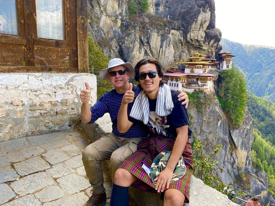 Deux personnes posant avec les pouces levés près d'un monastère à flanc de falaise.