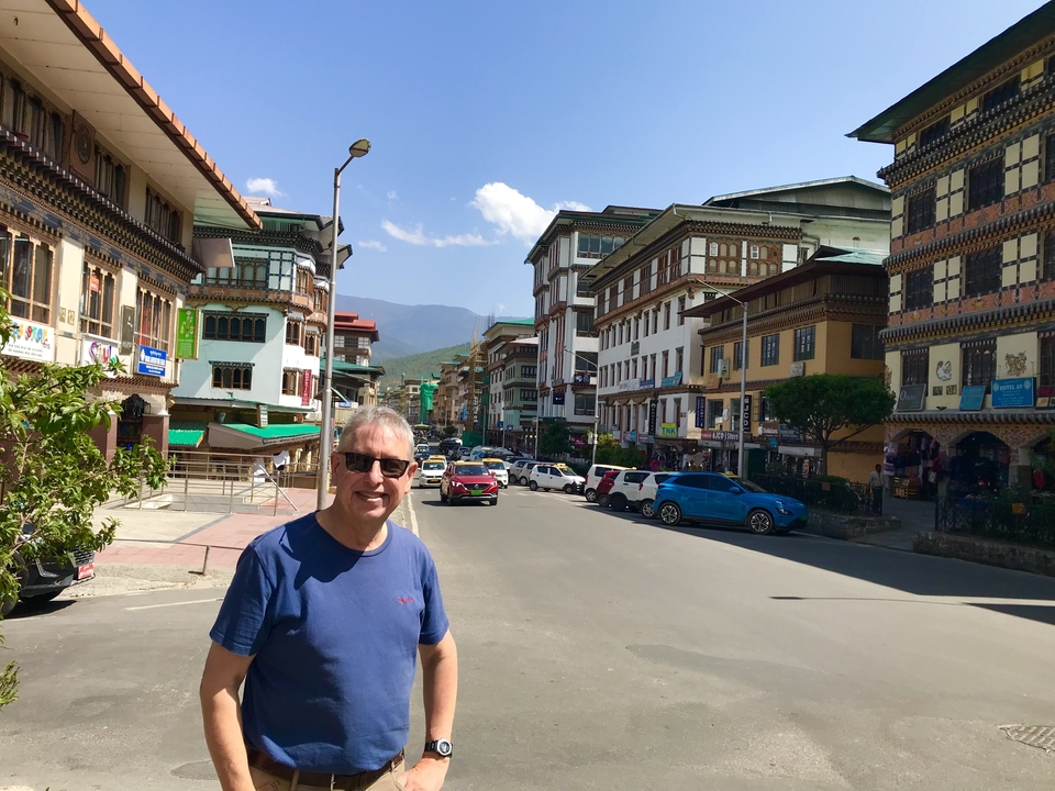 Rue avec des bâtiments bhoutanais traditionnels et un homme qui pose.