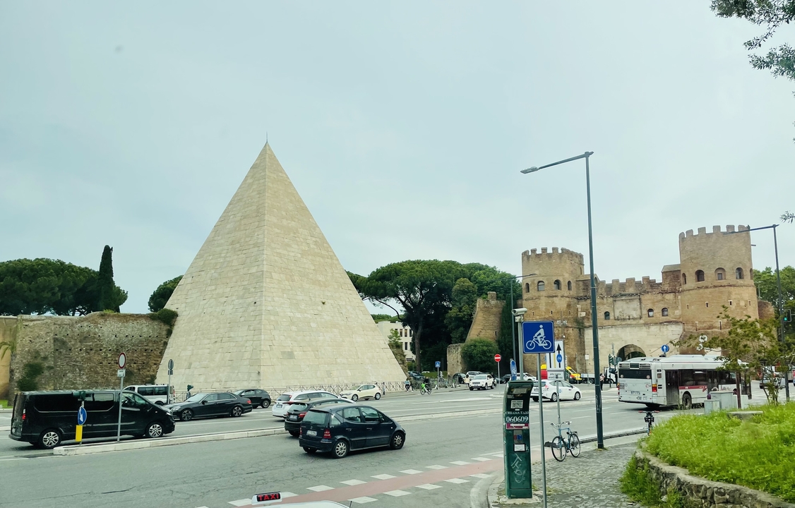 Pyramide de Cestius et Porta San Paolo à Rome, Italie avec des voitures et des gens autour.