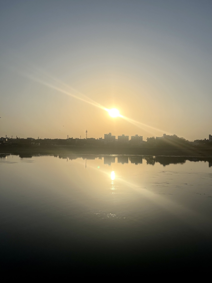 Sunrise over a river with urban skyline view.