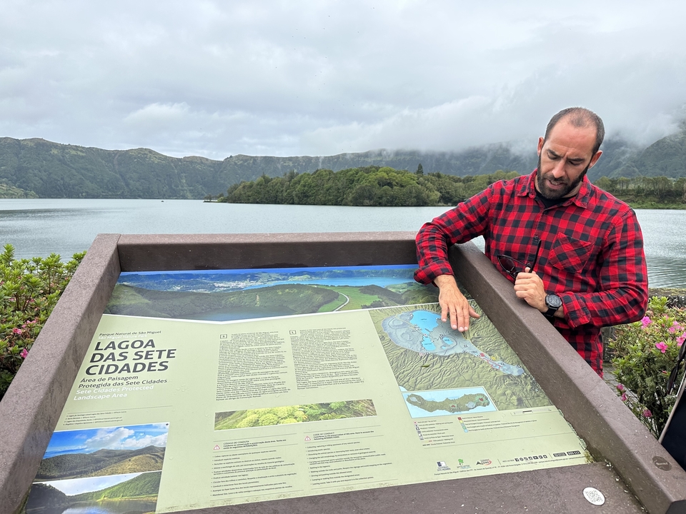 Homme montrant une carte de Lagoa Das Sete Cidades avec une vue sur le lac en arrière-plan.