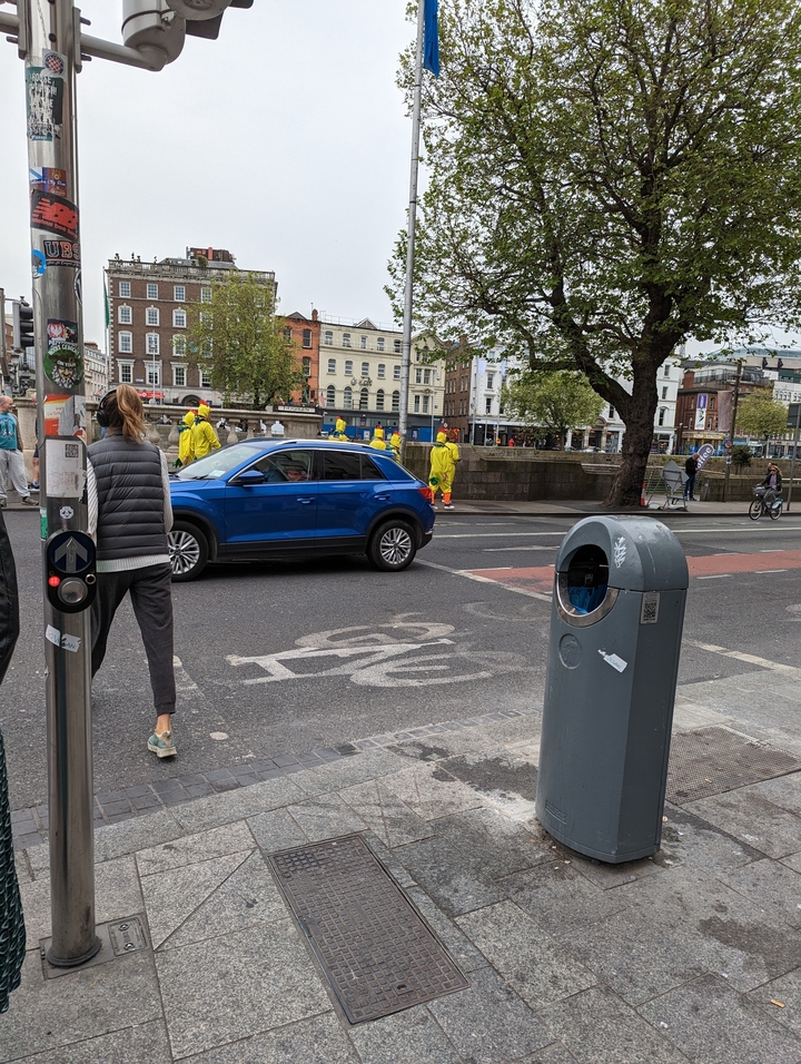 Scène de rue avec des gens et une voiture bleue.