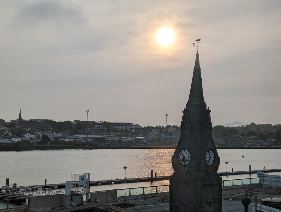 Tour d'horloge avec une rivière en arrière-plan au coucher du soleil.