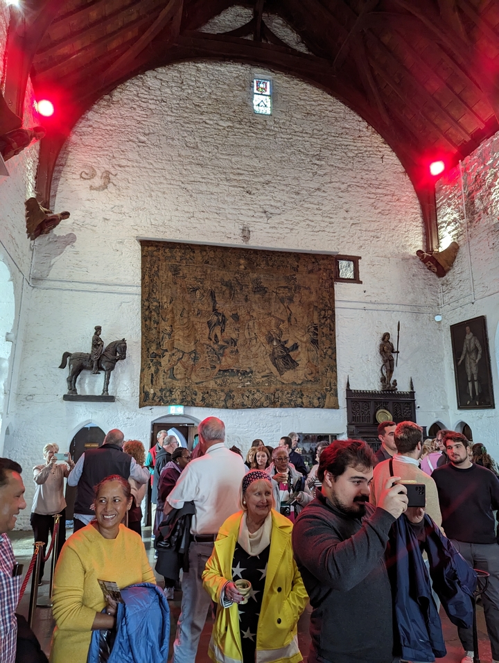 Des gens se sont rassemblés dans une salle historique avec des œuvres d'art au mur.