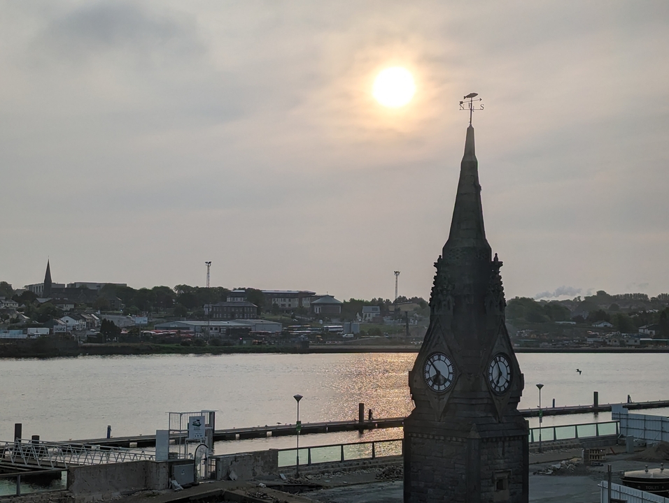 Tour d'horloge avec une rivière en arrière-plan au coucher du soleil.