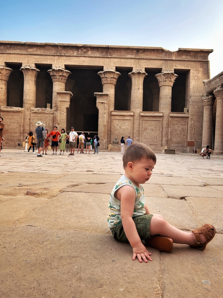 Enfant assis devant des structures égyptiennes antiques avec des gens autour.