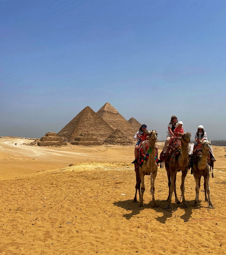 Groupe de personnes à dos de chameau devant des pyramides dans le désert.