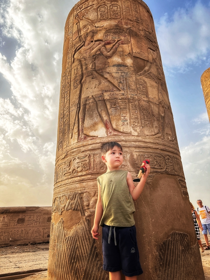 Enfant tenant un jouet à côté d'une colonne égyptienne antique.
