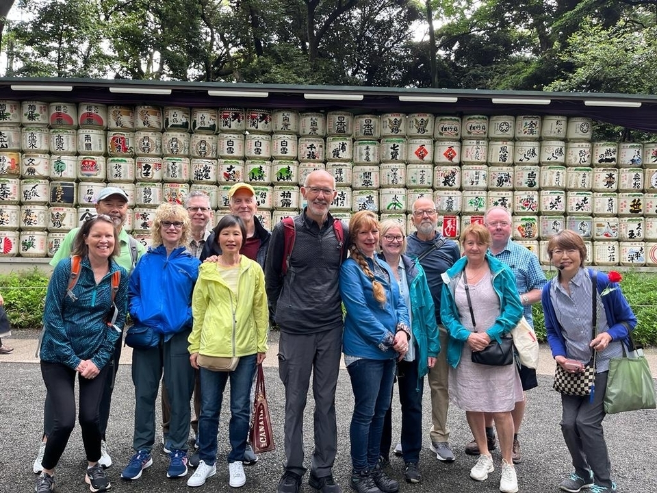 Groupe de personnes posant devant un mur de tonneaux de saké