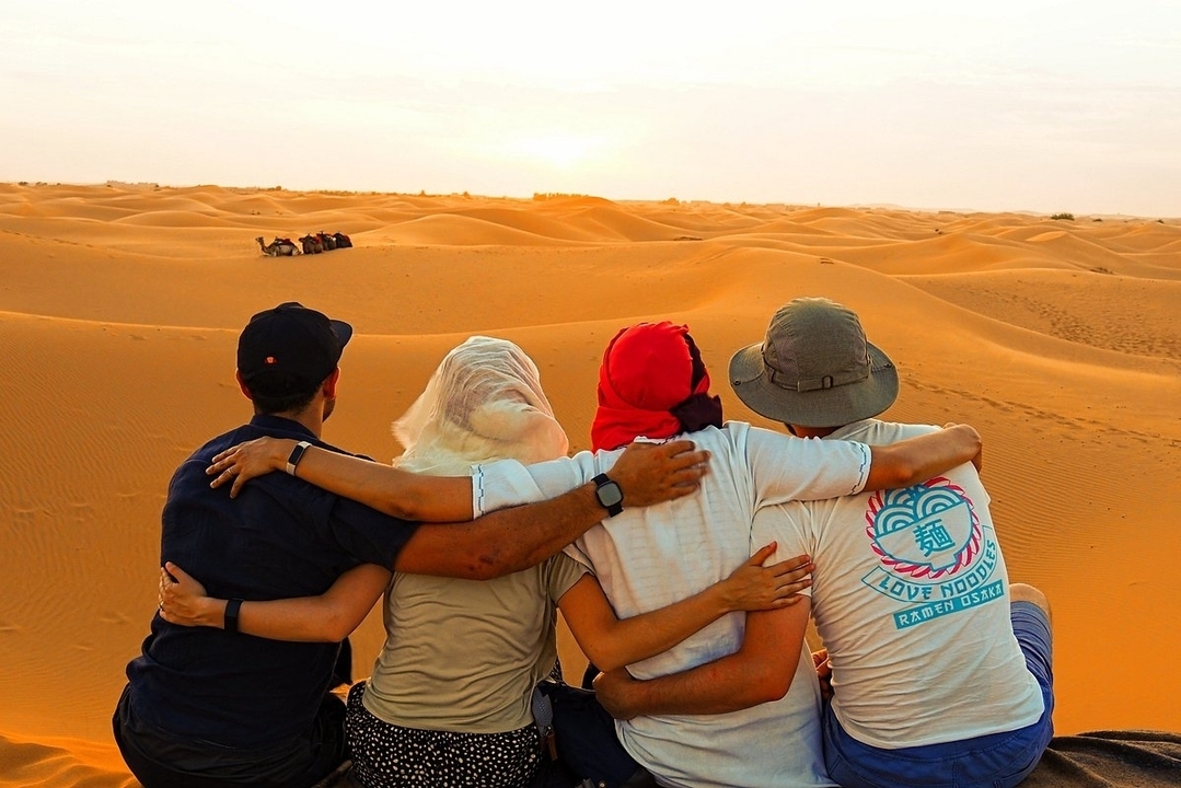 Groupe de personnes assises dans le désert observant des chameaux au coucher du soleil.
