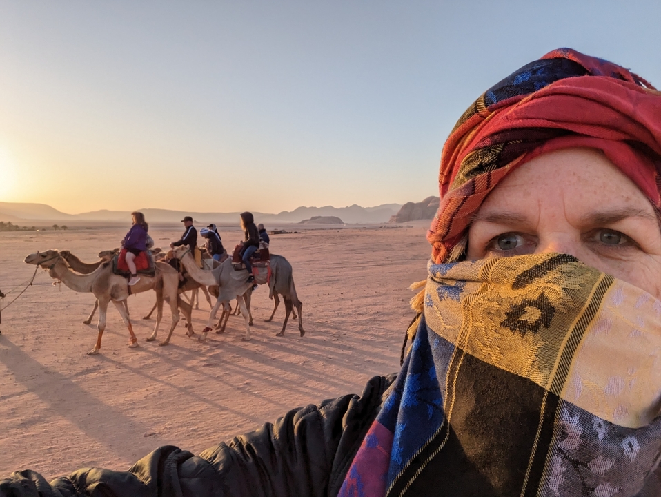 Promenade à dos de chameau avec une personne en tenue traditionnelle dans un paysage désertique au coucher du soleil.