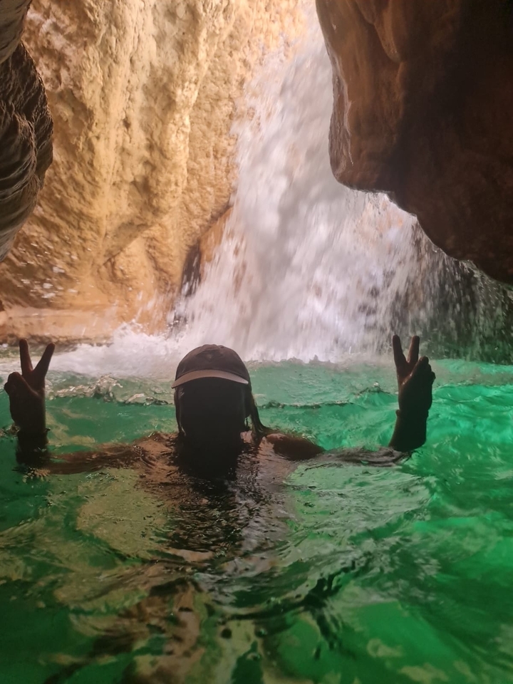 Personne dans l'eau à l'entrée d'une grotte avec une cascade en arrière-plan.