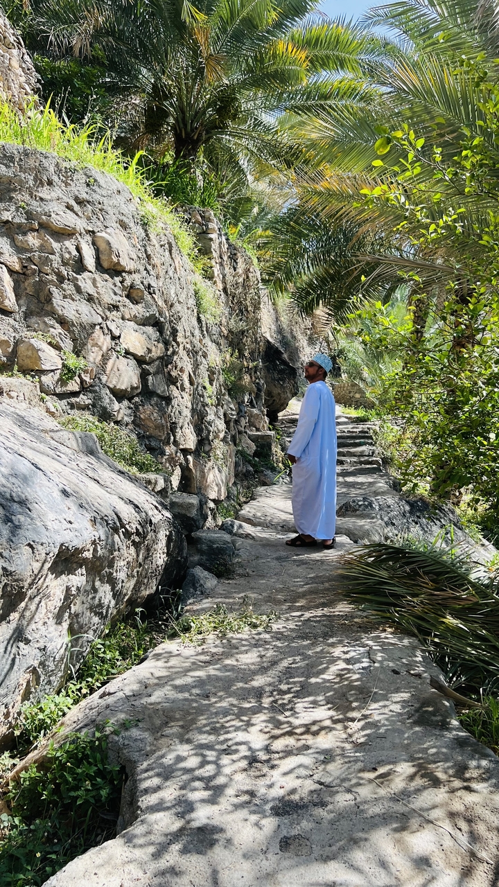 Homme en tenue traditionnelle marchant sur un sentier de pierre le long d'une falaise rocheuse.