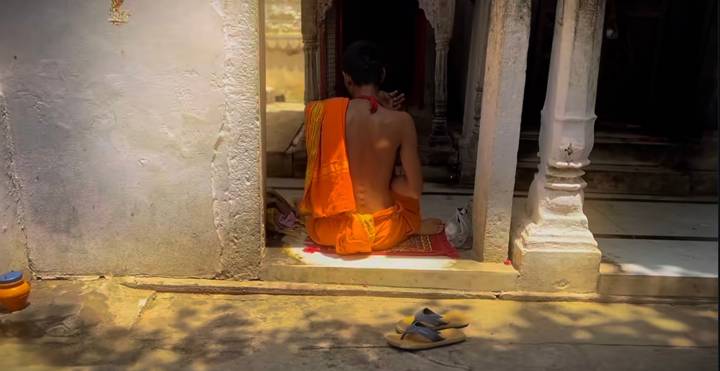 Personne assise sur une marche en tenue traditionnelle à côté d'une paire de sandales.