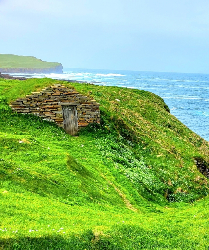 A stone hut in a lush coastal landscape.