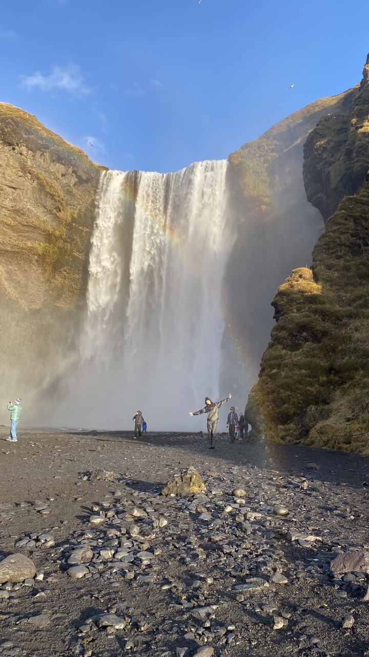 Visitors standing near a large waterfall with a rainbow