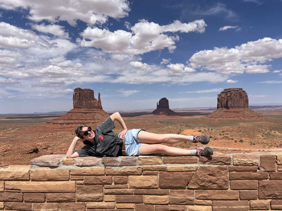 Person posing on a wall with Monument Valley in the background.