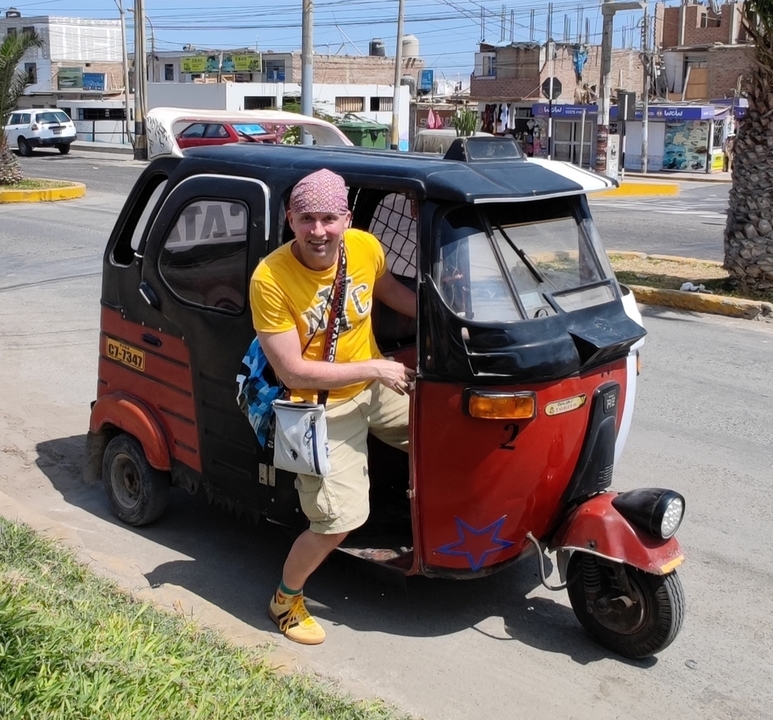 Personne sortant d'un tuk-tuk rouge et noir dans une zone urbaine.