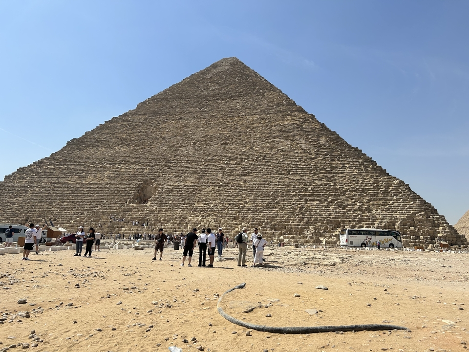 Un grand groupe de touristes près de la base d'une pyramide, avec des véhicules en arrière-plan.
