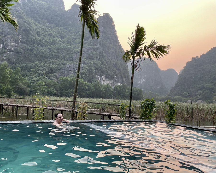 Personne nageant dans une piscine avec un arrière-plan montagneux luxuriant au coucher du soleil.