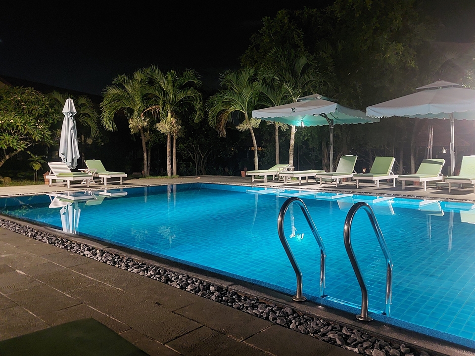 Piscine illuminée entourée de transats et de palmiers la nuit.