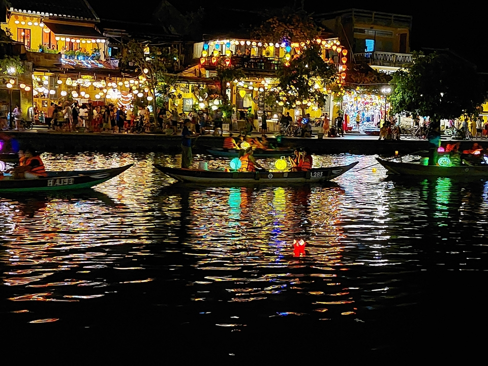 Des bateaux avec des lanternes colorées flottant sur une rivière pendant un festival.