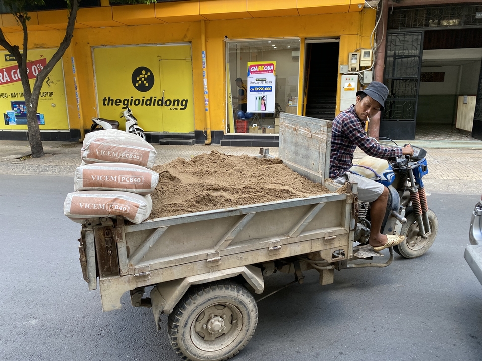 Homme conduisant une remorque de moto transportant des sacs de sable dans une ville.
