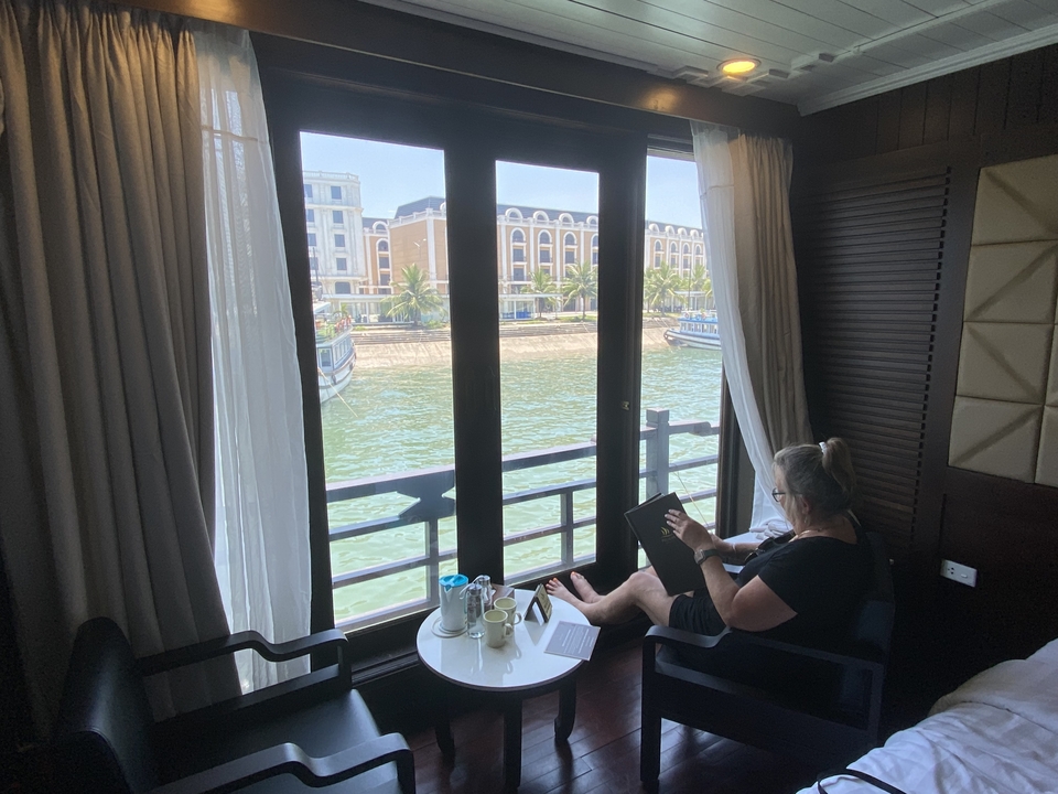 Personne lisant dans une chambre d'hôtel avec un balcon donnant sur l'eau.