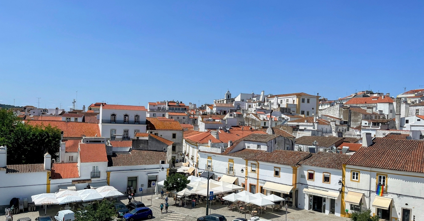 View of a town plaza with red-tiled roofs and outdoor umbrellas.