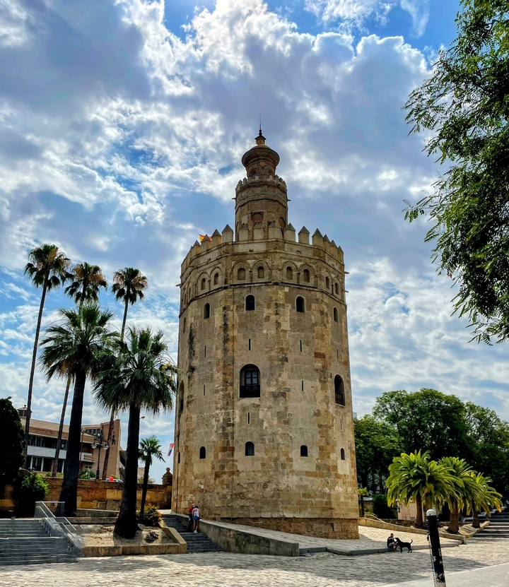 Circular tower surrounded by palm trees under a cloudy sky.
