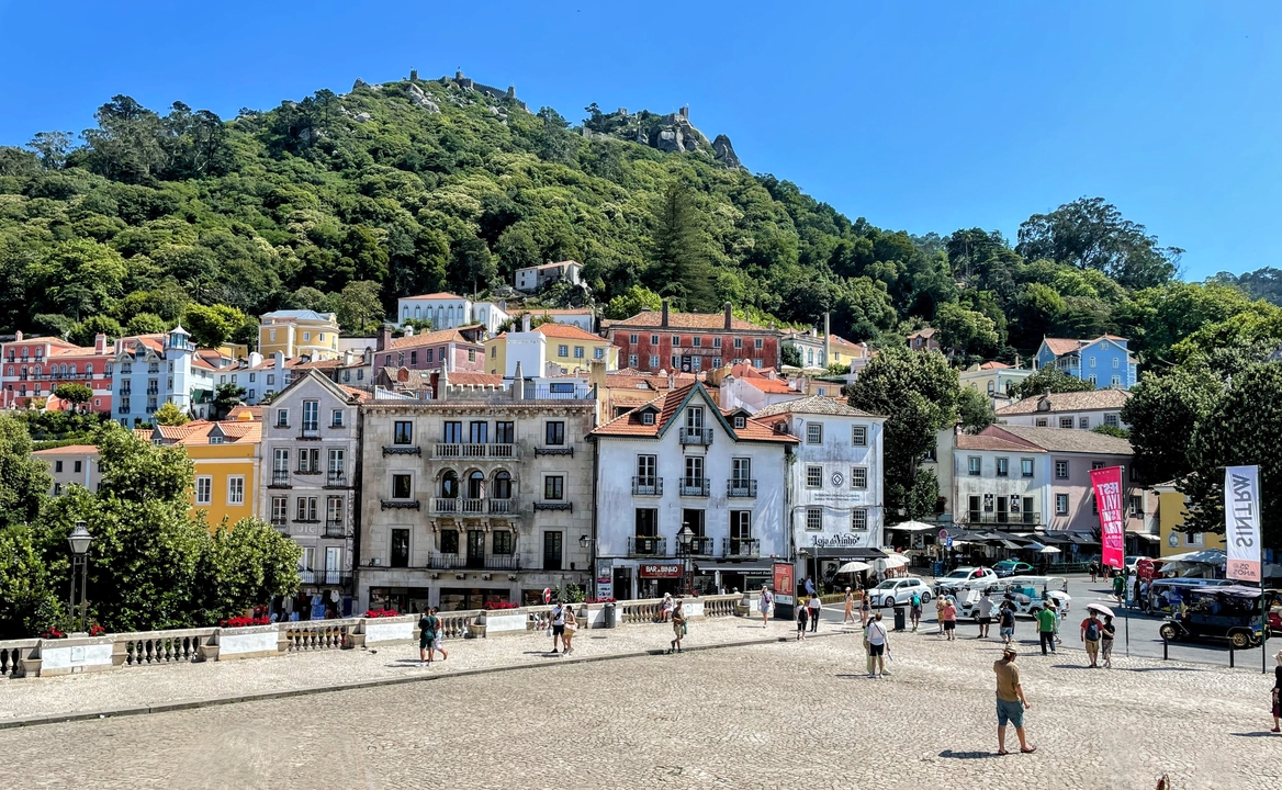 Colorful hillside town square with tourists and greenery.