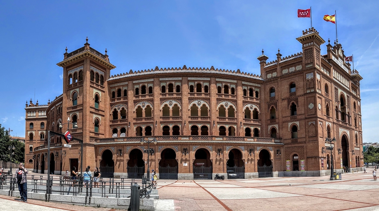 Exterior of a large brick bullring with flags on a clear day.