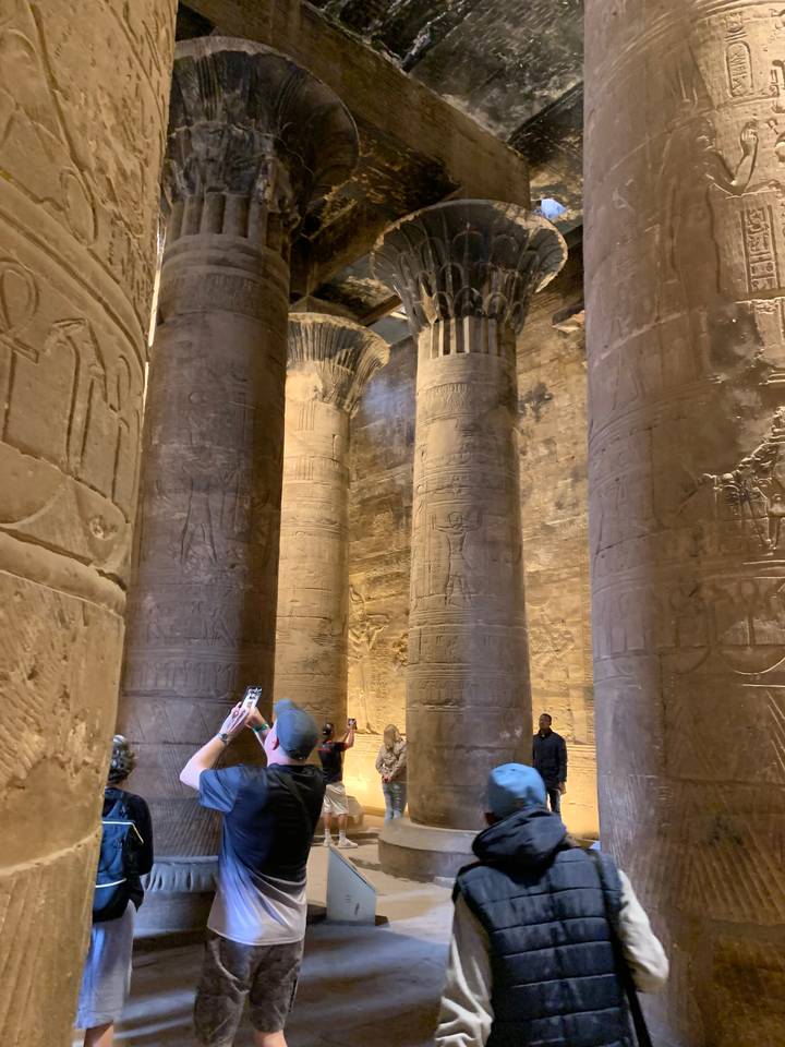 Interior of an ancient structure with columns and visitors.