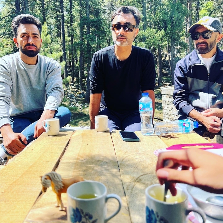 Trois personnes assises autour d'une table en bois à l'extérieur.