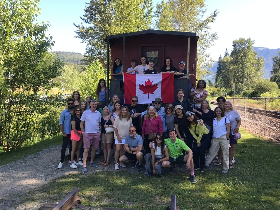Groupe tenant un drapeau canadien devant un wagon de train.