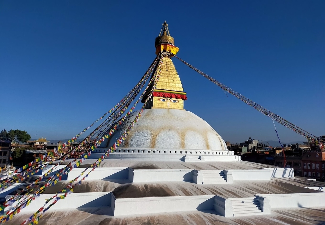 Stupa de Boudhanath avec drapeaux de prière contre un ciel bleu dégagé.