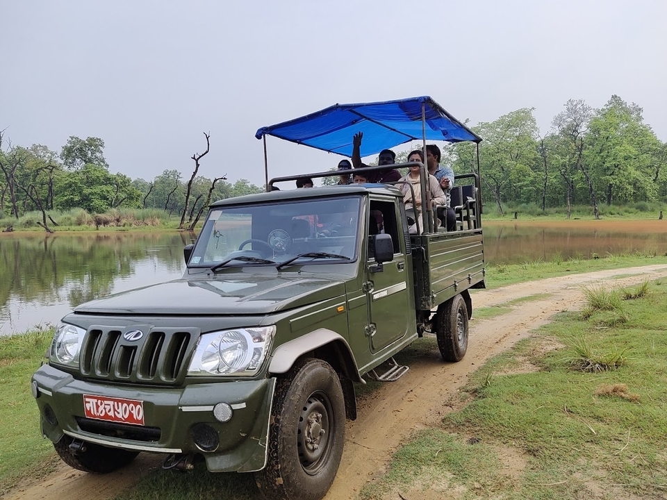 Véhicule de safari avec des personnes conduisant à travers un parc naturel avec un lac.