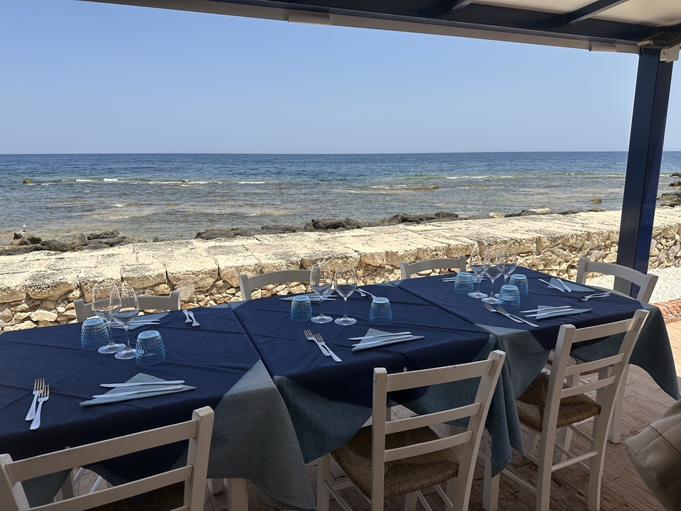 Cadre de restauration en plein air au bord de mer avec une nappe bleue et des chaises.