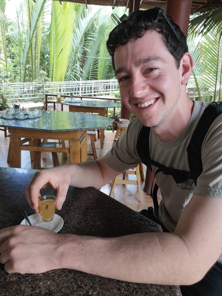 Personne souriante tenant un petit verre dans un café en plein air.