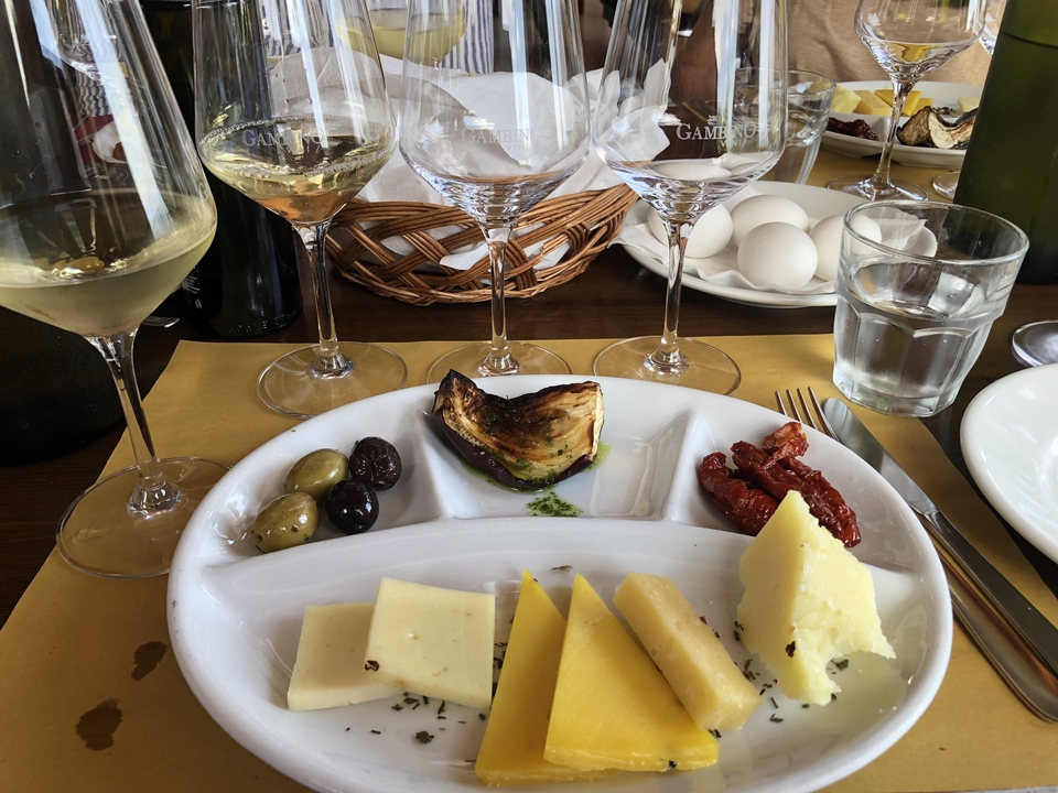 Une assiette de fromages assortis et de légumes accompagnée de verres de vin.