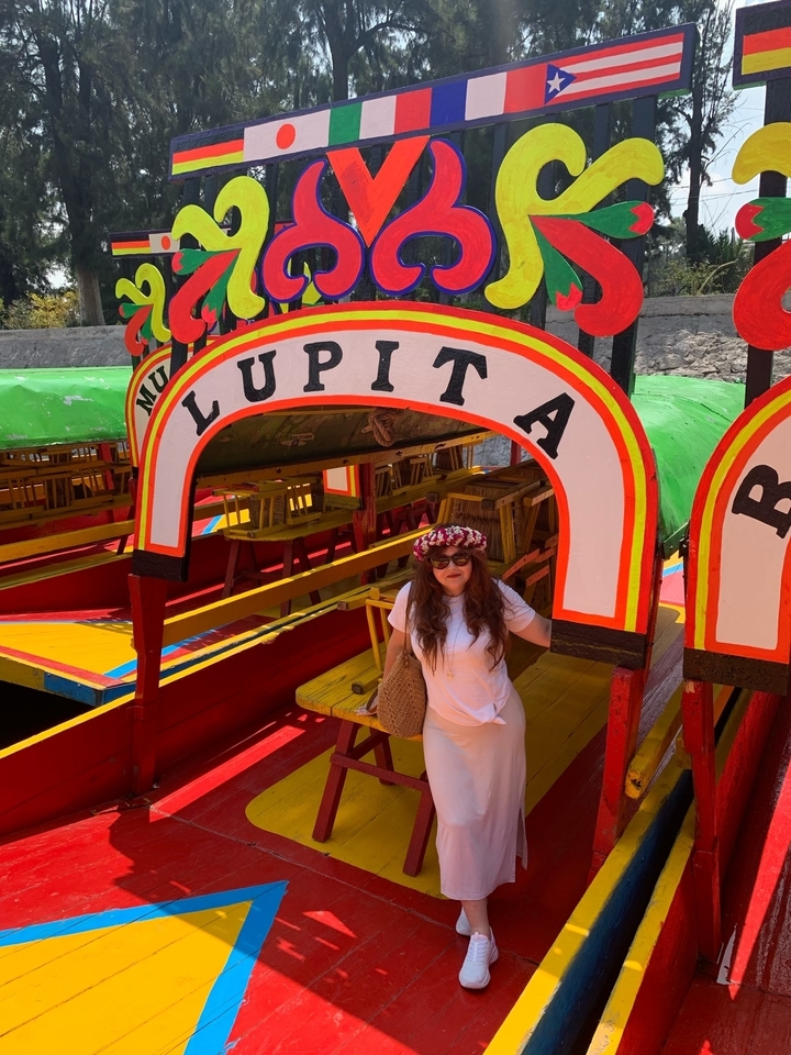 Une personne posant à côté d'un bateau coloré nommé 'LUPITA'.