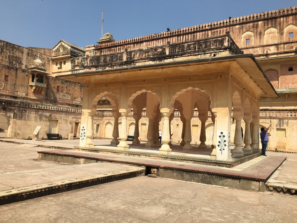 Bâtiment historique avec des arches dans une cour, personne debout à proximité.